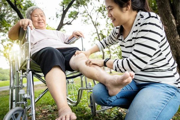 Asian senior mother in wheelchair,receiving a leg massage from her daughter,old woman enjoy,pain relief,elderly people suffer from sore muscles,female caregiver use a gentle massage hand to relaxation