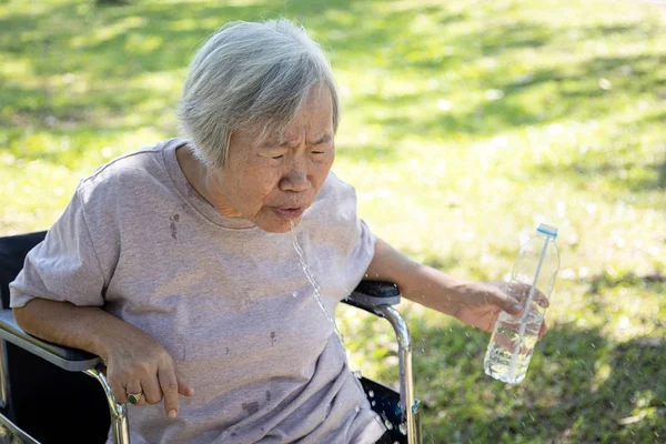 Asian senior woman choking on water,elderly people with poor  quality water,bad smell and dirty of water, smelled plastic causing her to spitting out the water while drinking from plastic bottles — Stockfoto