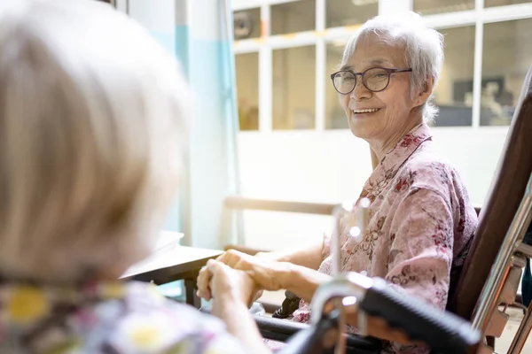 Sonriendo asiática mujer mayor está feliz de conocer accidentalmente a su amigo cercano o buenos viejos amigos en el hospital, pacientes ancianos en silla de ruedas tomados de la mano para hablar junto con la nostalgia, la verdadera amistad — Foto de Stock