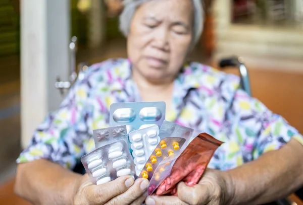 Sick senior woman holding medicine pills  in wheelchair,sad  female elderly showing a lot of drugs,medication to treatment her condition,asian old people is tired of having take medicine every day — Stockfoto