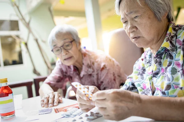 Asiatiska kvinnliga senior hold medicin piller, äldre kvinna konsultera sina gamla människor vän, hjälp och läsa medicin etiketter läkemedel recept, diskutera läkemedel som mottagits från sjukhuset, bruksanvisningar — Stockfoto