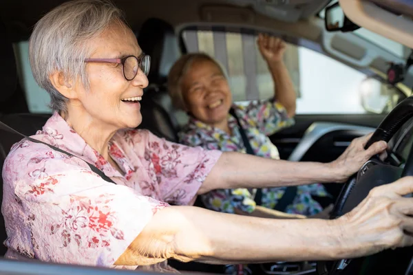 Happy asian senior female driver in her car,enjoy traveling during retirement age with her friend,healthy old people having fun,laughing together,elderly woman driving car,road trip,travel concep
