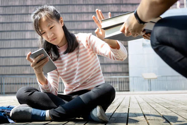 Asian child girl is avoiding reading book, say no,she wants to use a mobile phone to play games or chat with friends, teenage daughter is refusing to read books from her mother, education concept