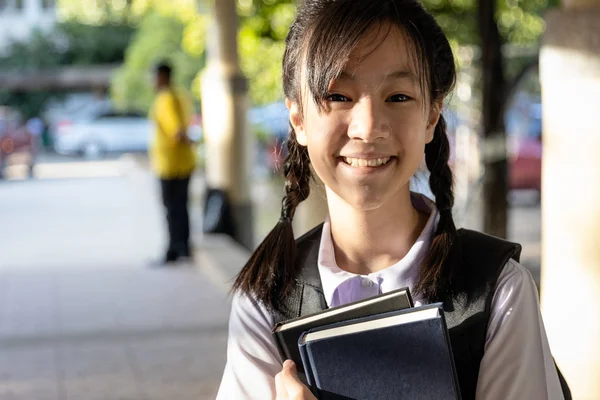 Smiling child girl with backpack on her back,holding a books on her arms going to school,cheerful schoolgirl wearing a school uniform,happy asian teenage student with bag,back to school concept