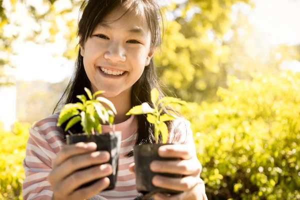 Smiling and happy asian child girl holding seedling,small trees for planting,female teenage showing young green plant in nature, campaign or help grow trees to reduce global warming,world environment day,earth day — Stock Photo, Image