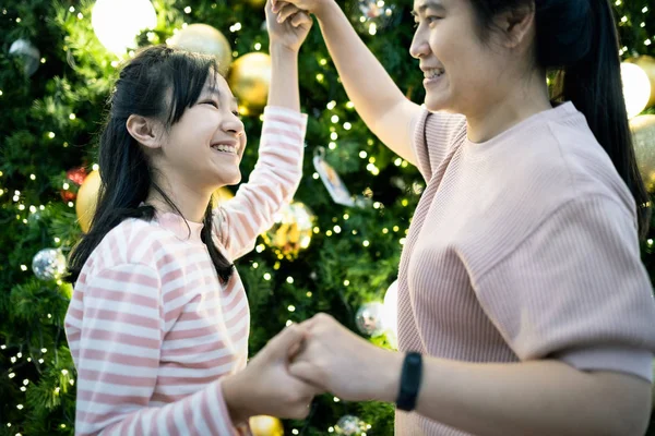 Belle femme souriante, fillette dansant autour d'un arbre de Noël décoré, avant la veille du Nouvel An à la maison, mère aimante, fille asiatique s'amuser, se sentir heureuse, arbre de Noël de fête lumières arrière-plan — Photo
