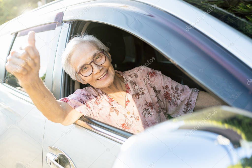Happy asian senior female driver with a smiling in her car, enjoying traveling during retirement age,healthy old people feel fun,elderly woman driving car, giving a thumbs up, road trip,travel concept