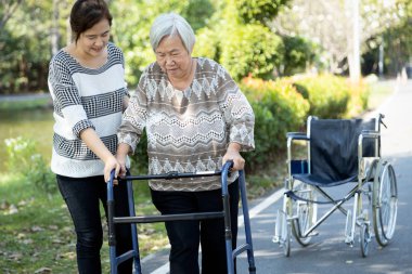 Asyalı yetişkin kadın ya da kız desteği, yaşlı anneye tekerlekli sandalyeden kalkması için yardım etmek, yaşlı mutlu bir hastanın rehabilitasyon sırasında yürüteç kullanması, kadın bakıcı ile yürüyüş çalışması, sağlık konsepti