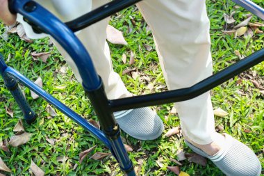 Yürümeye çalışan üst düzey Asyalı kadın hasta rehabilitasyon sırasında yürüyüş yardımı kullanıyor, güvenlik için Walker 'la yalnız yürüyen yaşlı kadın, parkta çimlerde yürüme pratiği yapıyor, engelli konsepti, yakın plan.