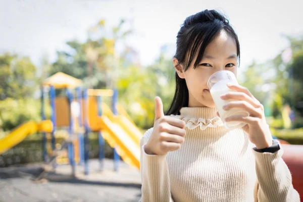 Ευτυχισμένο όμορφο κορίτσι από την Ασία, πίνει ένα ποτήρι γάλα, εμφανίζεται. — Φωτογραφία Αρχείου