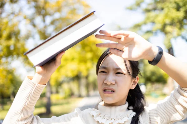 Asian child girl hold a book covering the sun to prevent facial — Stock Photo, Image