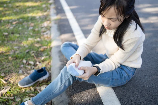 Asian child girl sitting on the floor and takes off a sneakers,,hold her sore spot,sad female teenage rubbing and massaging her painful foot,fatigue,achy and tired from walk,run or stand for a long day — ストック写真