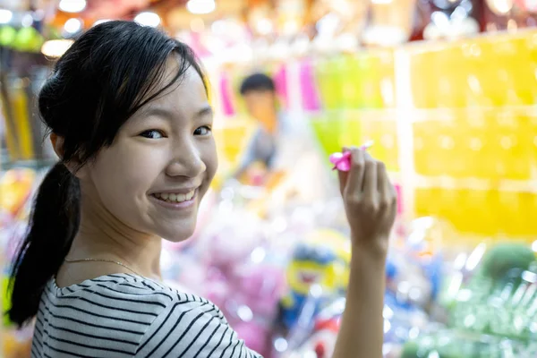Felice sorridente ragazza asiatica bambino in possesso di un dardo, guardando la fotocamera, divertirsi, adolescente femminile giocare il gioco di freccette con palloncini per un carnevale di notte, il festival annuale in città, Bangkok, Thailandia , — Foto Stock