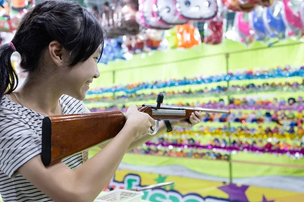 Glad leende asiatisk barn flicka som håller trä pistol, sikta till punkt, skjuta målet, kvinnlig spela skytte spel för en karneval på natten medan du besöker den årliga festivalen i staden, Bangkok, Thailand — Stockfoto