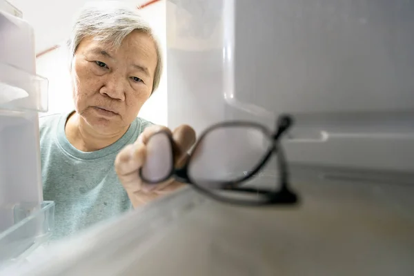 Mujer mayor asiática con síntomas de deterioro de la memoria, olvídese de sus anteojos en el refrigerador o guarde anteojos en el refrigerador, ancianas con demencia, deterioro cognitivo, alzheimer, amnesia —  Fotos de Stock