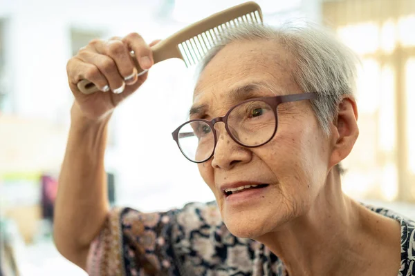 Primer plano de la cara de la gente mayor hermosa cepillando el pelo con peine en su mano, mujer mayor asiática feliz disfrute peinando el cabello, pelo limpio y saludable de la mujer, mujer anciana cuidar su cabello, concepto de belleza —  Fotos de Stock