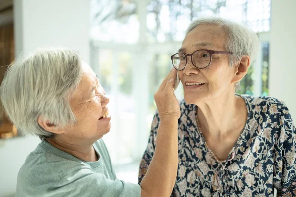 Sonriente asiático mujer anciano limpiar sudor en la cara de la piel de la hermana mayor y hablar felizmente, las personas mayores visitaron a su anciana en casa con nostalgia y preocupación, relación familiar, vida —  Fotos de Stock