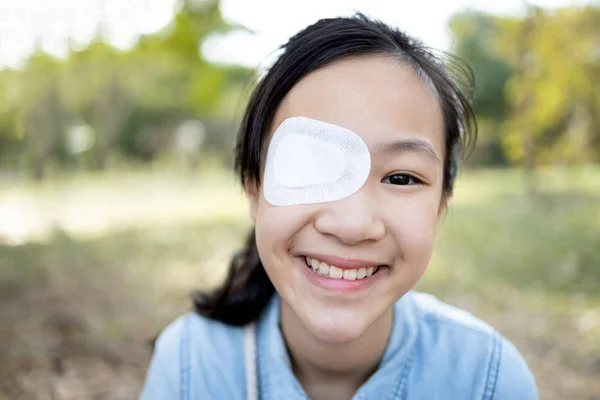 Mutlu Asyalı kız çocuğu ameliyattan ya da Strabismus tedavisinden sonra gözleri bandajlı gözlerle kapanıyor, tembel göz, hijyenik, enfeksiyonu önlüyor, tozu koruyor, gülümseyen kadın hastalar acı çekiyor, göz yaralanması geçiriyor. — Stok fotoğraf