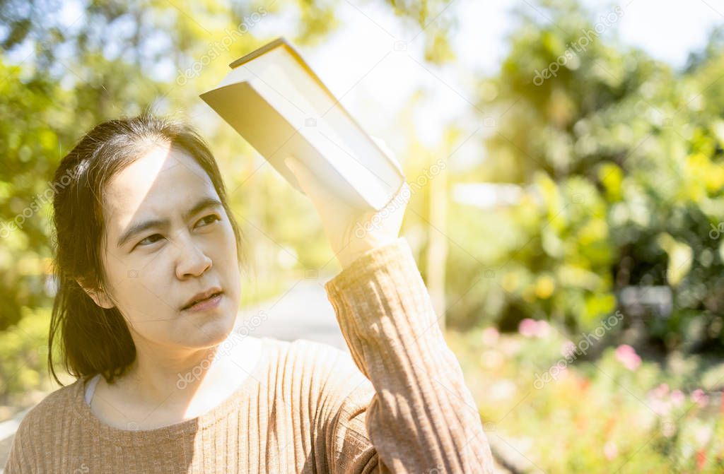 Asian woman hold a book covering the sun to prevent facial skin 