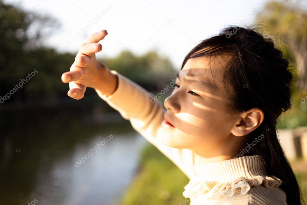 Asian child girl covering face by hand to protect,prevent face  skin from bright sun in outdoor summer,female people hand covered the strong sun light feeling hot uncomfortable,risk of eyes damage 