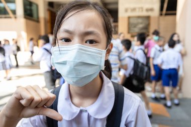 Asian child girl student thumbs down wearing medical face mask  in school,epidemic,spread of germ,Coronavirus,MERS-CoV,air contamination,Wuhan coronavirus 2019-nCoV, concept of Corona virus quarantine clipart