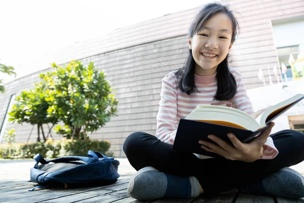 Asian teenage girl student holding a book in her hands and preparing for the exam reading book,schoolgirl reading textbook outdoor at school and looking at camera,concept of education,exam preparation