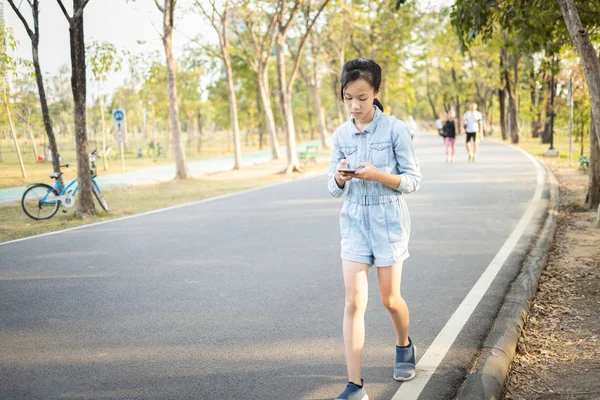 Ασιατική έφηβος κορίτσι είναι άρρωστος με τον εθισμό στο παιχνίδι; παίζουν σοβαρά τα παιχνίδια σε ένα έξυπνο τηλέφωνο, ενώ το περπάτημα στο δρόμο; πρόβλημα με εθισμένος στο online παιχνίδι των παιδιών; εθισμένος στο κοινωνικό δίκτυο — Φωτογραφία Αρχείου