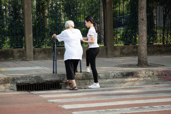Азійська старша жінка намагалася піднятися по тротуару з ходунками після перетину дороги на перехресті, рівень стежки вище, ніж дорога, інший рівень підлоги, проблеми літніх людей або інвалідів. — стокове фото