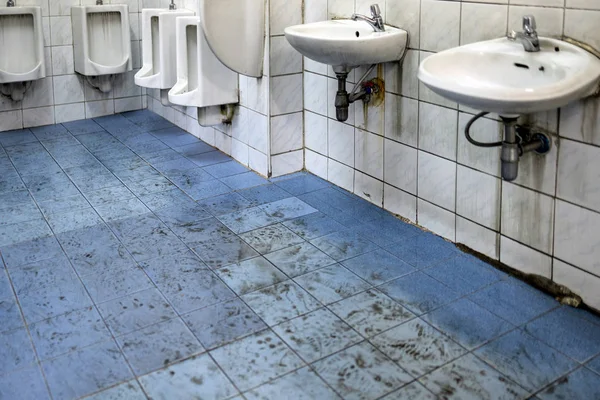 Old scruffy toilet where the floor is wet and filled with dirty footprints of student,filthy of urinals,washbasin,tiled wall, unhygienic,dirty restroom or has not cleaned the bathroom,back to school Royalty Free Stock Photos