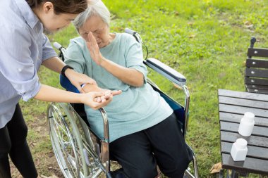 Injured asian senior woman wearing elbow support suffering from sore muscle,elbow joint arm pain,female caregiver do not intend to massage hard,unhappy elderly with elbow protector pads feeling hurt 