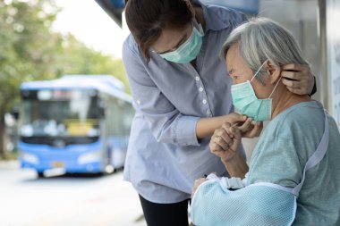 Yaşlı kadın için tıbbi maske takan Asyalı kadın öksürük ve ateşi olan yaşlı kadın otobüs durağındaki diğer insanlara, Coronavirus, Mers-Cov, Wuhan Virüsü 2019-ncov 'a mikrop bulaşmasını engelliyor. 