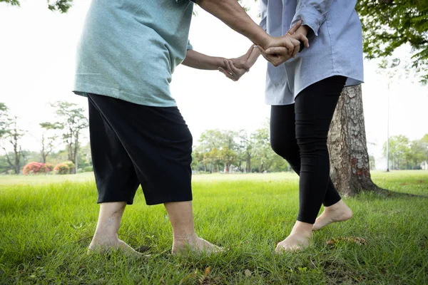 Asiática mujer mayor práctica caminar ejercicio con descalzo en la hierba para liberar la electricidad estática del cuerpo en el suelo, el cuidado de la hija, el apoyo de la madre anciana, saludable de los músculos del cuerpo y las piernas equilibrio — Foto de Stock