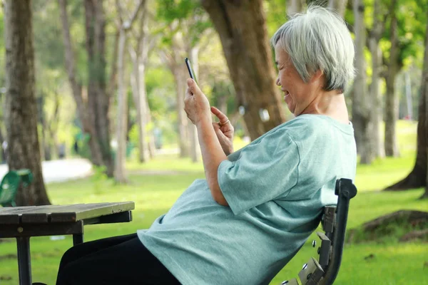 Mutlu Asyalı üst düzey kadın cep telefonu kullanıyor, ciddi ciddi akıllı bir telefonla oyun oynuyor, yaşlılar online oyununa bağımlı, sosyal ağa bağımlı, teknoloji, iletişim konsepti