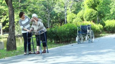 Asyalı yetişkin kadın ya da kız desteği, yaşlı anneye tekerlekli sandalyeden kalkması için yardım etmek, yaşlı mutlu bir hastanın rehabilitasyon sırasında yürüteç kullanması, kadın bakıcı ile yürüyüş çalışması, sağlık konsepti