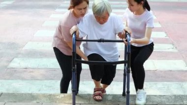 Asyalı anne ve kız yardım, bakım, destek, caddeden karşıya geçtikten sonra büyük anne, patika engeli, kaldırım uzun, farklı seviye alan, yürüteç, bacak ağrısı, yaşam tarzı sorunu olan yaşlı