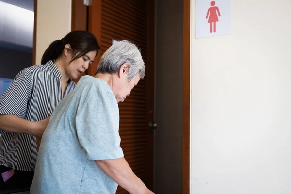 Pflegerin hilft älteren Frauen, vorsichtig auf die Toilette zu gehen, asiatische Senioren mit Blasenkontrollproblemen müssen auf die Toilette, alte Menschen leiden unter Stress Harninkontinenz — Stockfoto