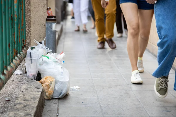 Rubbish on the pedestrian in city with people,litter garbage  plastic scrap on sidewalk,throw away,plastic bag waste on footpath,pollution,environmental problem,concept of throw trash in a trash can — Stock Photo, Image