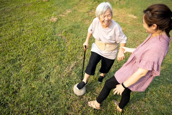 Жіночий доглядач і здорова старша жінка грають у футбол на відкритому повітрі вдома, розслабляються вправи зі старим футбольним м'ячем, щасливі усміхнені літні люди отримують задоволення разом, піклуються про старих людей — стокове фото