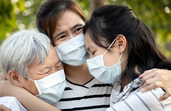 Medikal maske takmış depresyondaki Asyalı aile ağlıyor, kederden acı çekiyor, ailesinin büyük bir kaybı enfekte olmuş, salgınla mücadele ediyor, salgından etkilenmiş, sarılıyor, birbirlerini teselli ediyorlar.