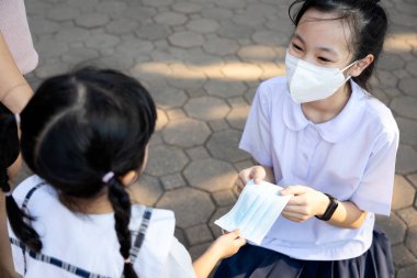 Tayland okul üniformalı cömert kız öğrenci maskesini küçük kızla paylaşıyor, hastalıkları, koronavirüsü, grip mevsimini, tozu, hava kirliliğini, Pm2.5 'u önlemek için koruyucu maske veriyor. 