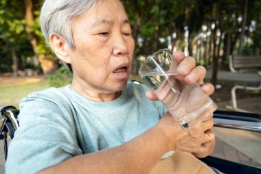 Asyalı son sınıf öğrencisi bir bardak su tutuyor, su içerken elleri titriyor, elleri titreyen yaşlı kontrolsüz vücut sarsıntıları, temel titreme belirtileri, Parkinson hastalığı, nörolojik bozukluklar.