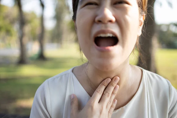 Close up of hands touching neck,sick asian girl has strong sore throat,cough,hoarseness,laryngeal cancer,swelling,young woman suffering from throat problems,tonsillitis,painful swallowing,health care