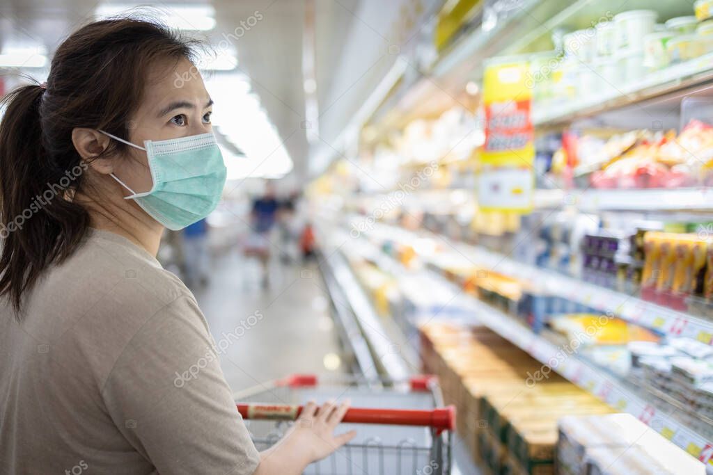Asian woman wear a mask,looking fresh water and milk,choosing necessary food products,people panic buying and hoarding during the Covid-19,Coronavirus epidemic,girl preparing for
