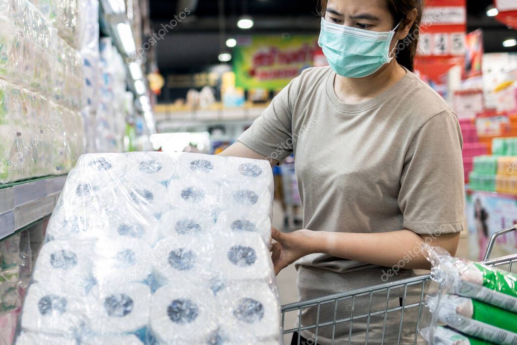 Asian woman wear face mask,chooses tissue paper,toilet paper while shopping food,people panic buying, hoarding during the Covid-19,spread of Coronavirus,girl preparing for pandemic,contagious disease