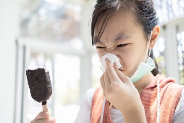 Sick asian child girl has runny nose and blows her nose into a tissue paper while eating too much ice cream,woman with illness from colds,seasonal flu,loss of taste and impaired sense of tasting food clipart