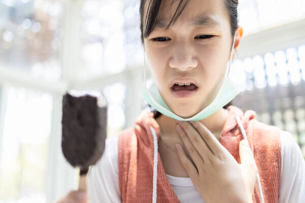 Sick asian child girl with a flu,dry cough and a sore throat,eating too much ice cream,loss of taste and sense of tasting food or illness from Coronavirus,Covid-19 infection symptoms,health problems