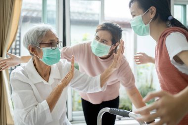 Maske takan, Covid-19 virüsü kapmaktan korkan, Coronavirus salgını olan Asyalı son sınıf öğrencisi yaşlı bir kadın elini kaldırıyor, ailesinin ona yaklaşmasını engelliyor.