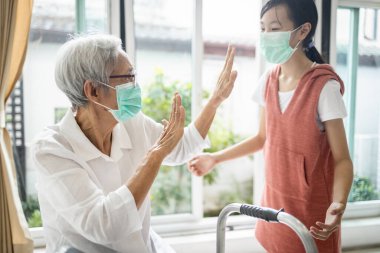 Asyalı çocuk torunu büyük büyükannesini kucaklamak üzere, yaşlılara yaklaşmaktan kaçınıyor, mesafeyi koruyor, grip enfeksiyonunu önlüyor, Coronavirus, Covid-19 salgını, sosyal mesafeler