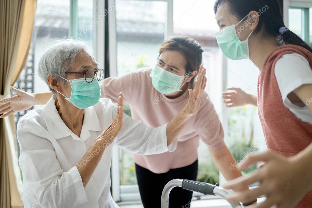 Asian senior woman wearing a mask,afraid of being infected with Covid-19,flu,contagion of Coronavirus,elderly is raising her hands,refusing,preventing her family from approaching her,social distancing