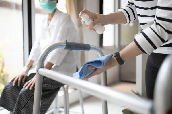 Alkol antiseptiği sıkan bir kadının elleri, yaşlı annesi için yürüme cihazlarını temizliyor Coronavirus salgını sırasında, Covid-19, yüzeyi dezenfektan spreyiyle temizliyor.